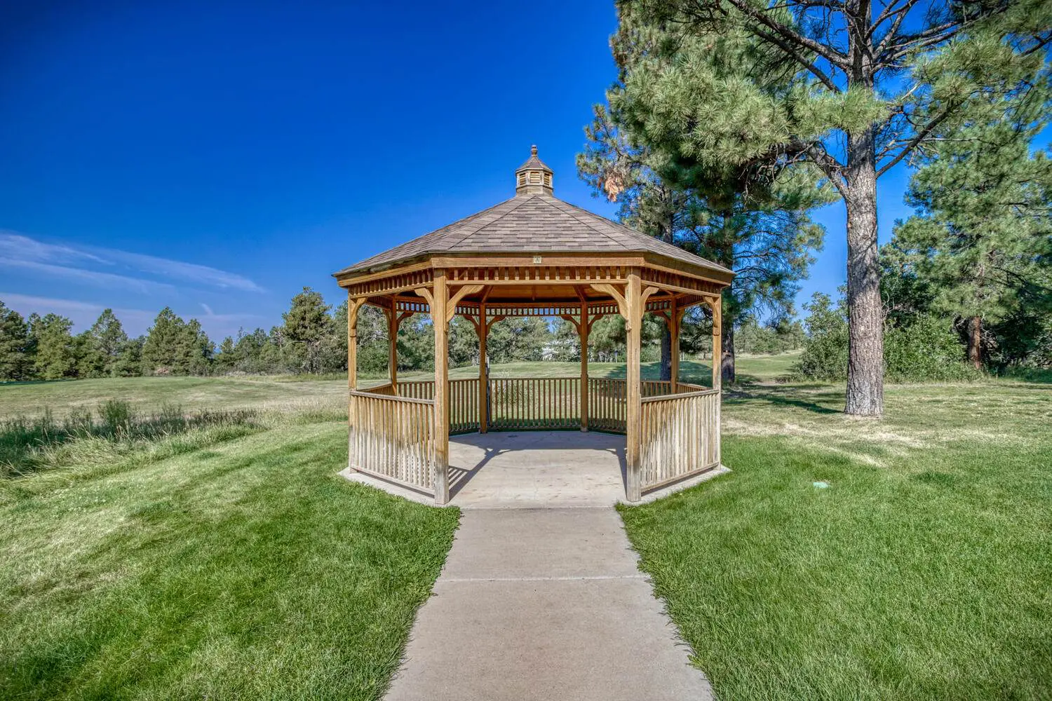 A wooden gazebo sits in the middle of a grassy area.