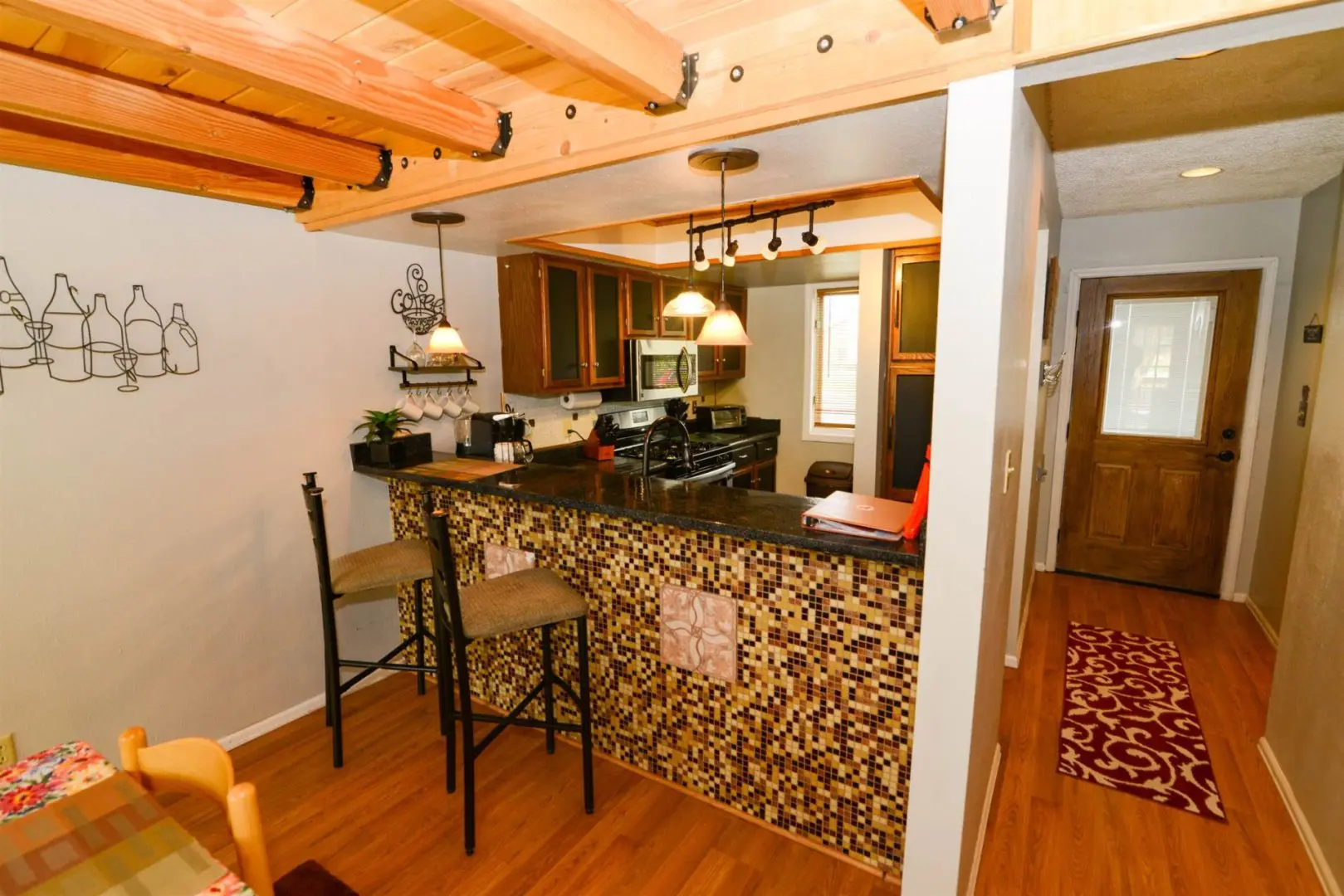 A kitchen with a bar stools and a wooden ceiling.