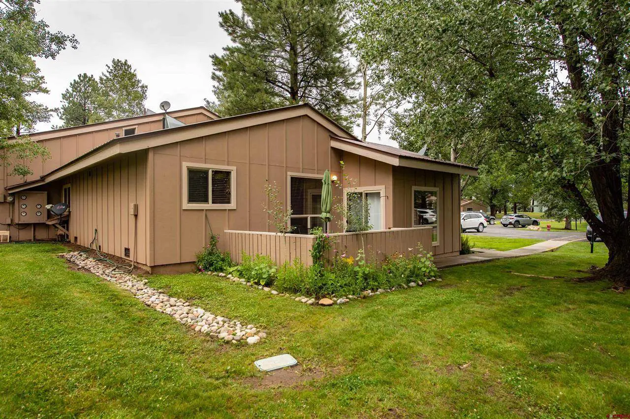 A tan home with grass and trees in front of it.