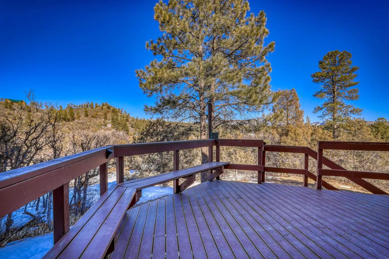 A wooden deck with a bench overlooking a wooded area.