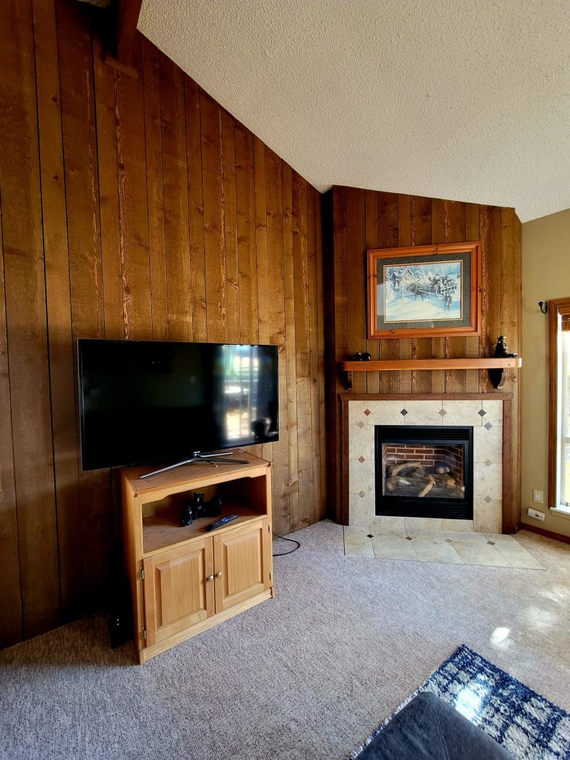 A living room with wood paneling and a fireplace.