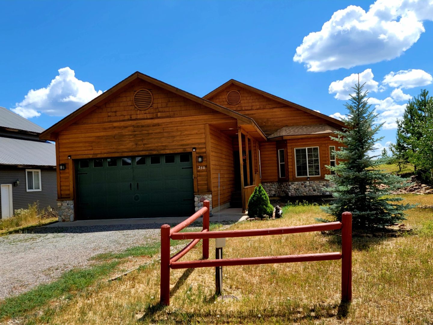 A house with a garage in the middle of a grassy field.