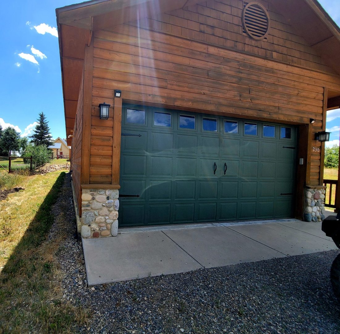 A green garage door in front of a log cabin.