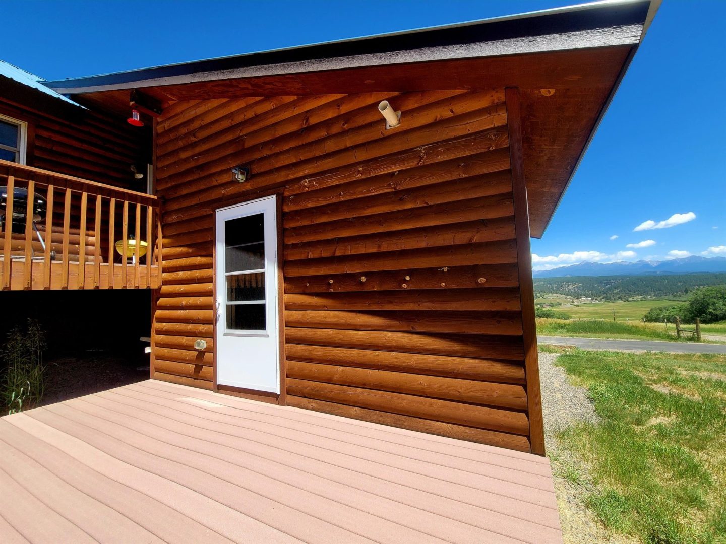 A log cabin with a deck and mountains in the background.