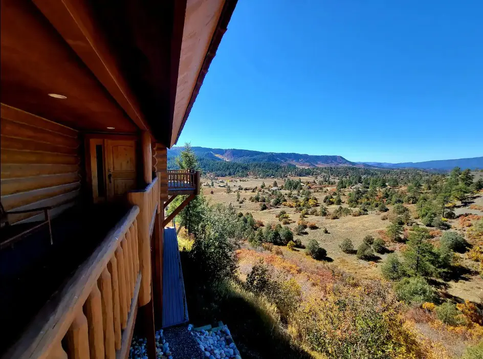 A view from the balcony of a log cabin overlooking a valley.