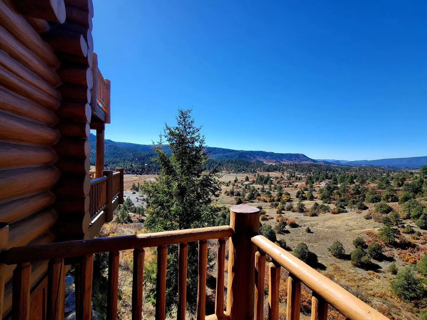 A view from the balcony of a log cabin overlooking a valley.