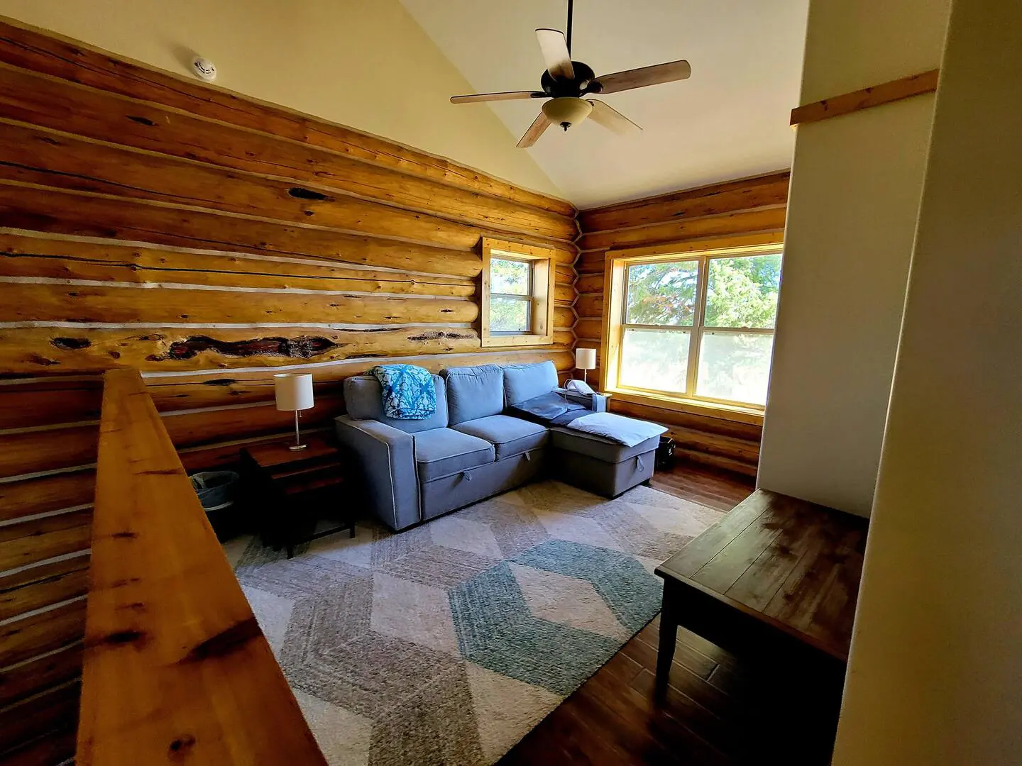 A living room in a log cabin with a ceiling fan.