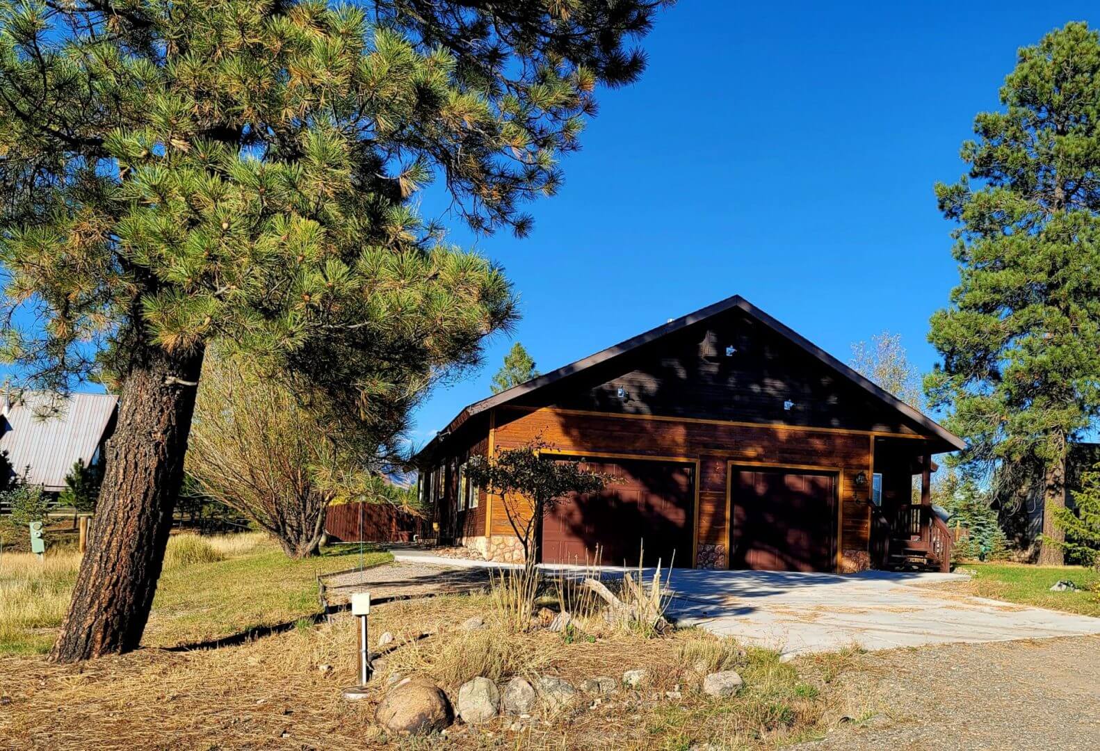 A log cabin with a driveway and trees in the background.